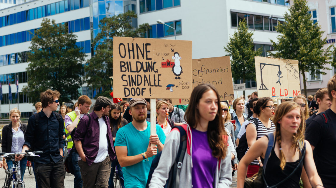 Zu sehen ist ein Ausschnitt einer Demonstration im Rahmen eines "Bildungsstreiks" 2014. Auf einem Schild steht: "Ohne Bildung sind alle doof".