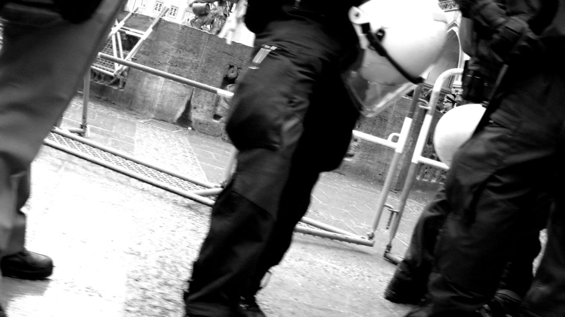 Zu sehen sind drei Bereitschaftspolizisten, fotografiert von unten und mit Helmen und Ausrüstung.