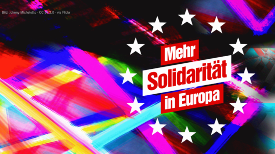 Zu sehen ist ein bunter, künstlerischer Hintergrund. Darauf die Sterne der Europa-Fahne und der Text "Mehr Solidarität in Europa"
