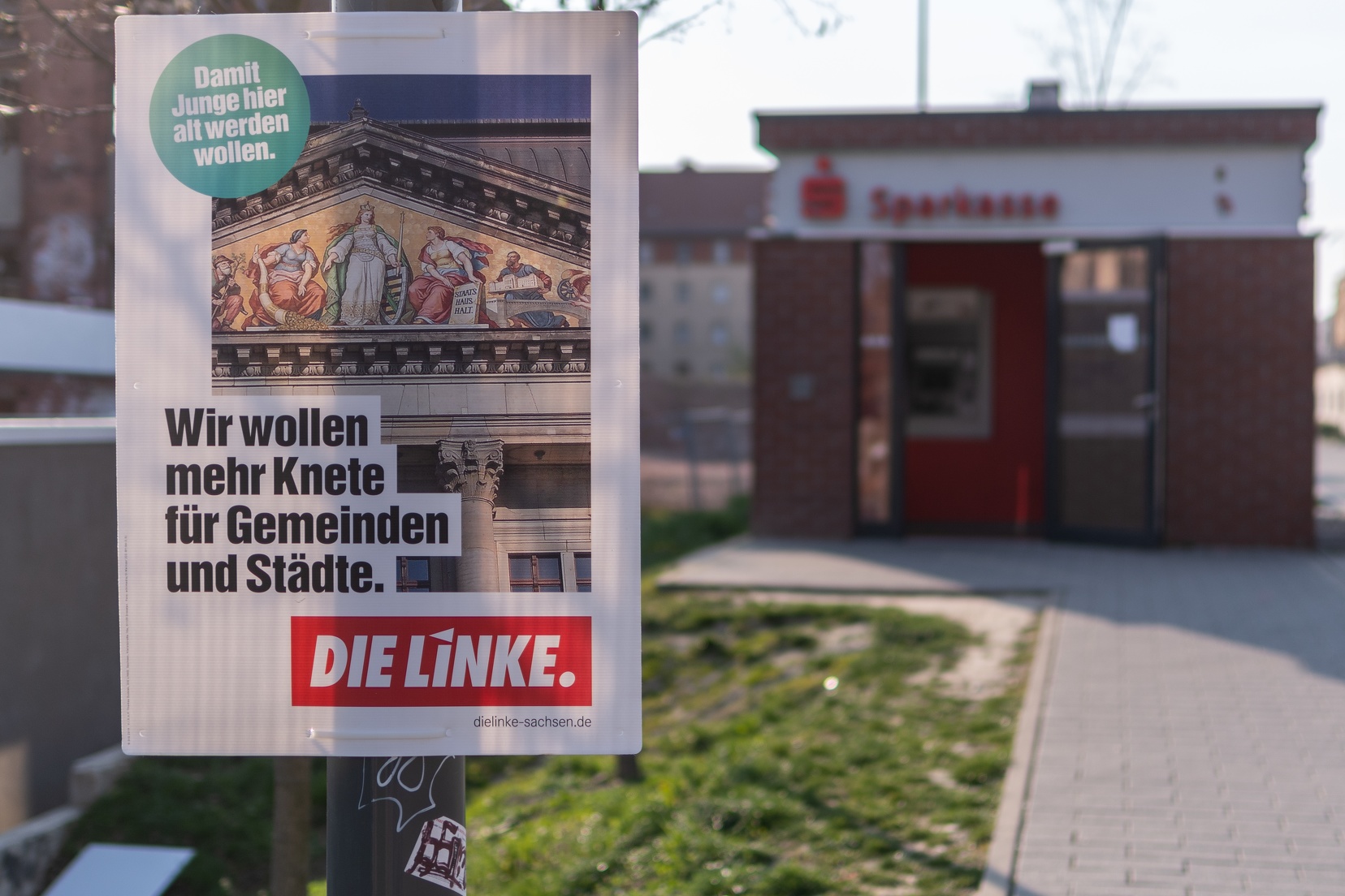 Zu sehen ist ein Wahlplakat mit dem Text: "Wir wollen mehr Knete für Gemeinden und Städte". Das Plakat hängt vor einer Sparkasse.