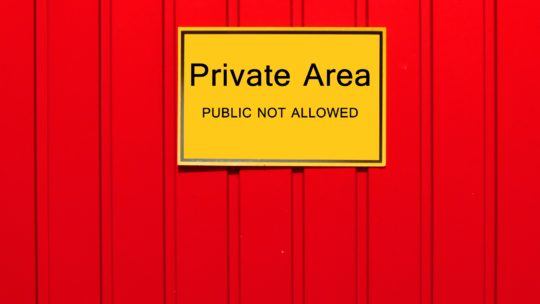 Auf dem Bild sieht man ein gelbes Schild auf einem roten Zaun. Auf dem Schild steht: "Private Area. Public is not allowed"