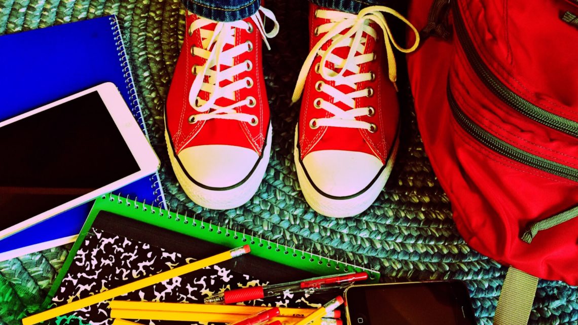 Zu sehen sind rote Schuhe eines Kindes umgeben von Stiften, Papier und einem Tablet