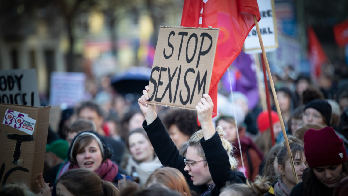 Foto von der Frauen*kampftagsdemo 2019, bei der eine Teilnehmerin ein Schild mit dem Text "Stop Sexism" hochhält