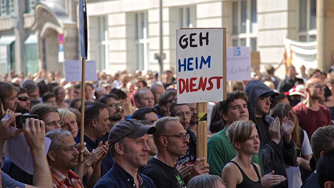Demonstration auf der jemand ein Schild mit der Aufschrift: "GEH HEIM DIENST" trägt.