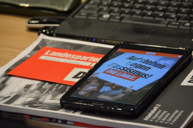 Zu sehen sind ein Laptop, eine Stimmkarte, ein Heft und ein Tablet - vermutlich Parteitags-Unterlagen