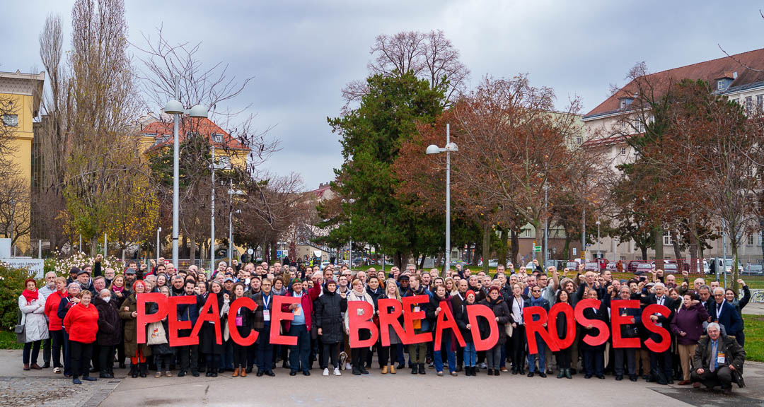 Delegierte des EL Kongresses von Ende 2022 halten die Buchstaben "Peace Bread Roses"