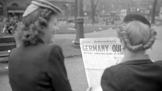 Zwei Frauen lesen auf einem Foto von hinten fotografiert die Zeitungsüberschrift "Germany quits"