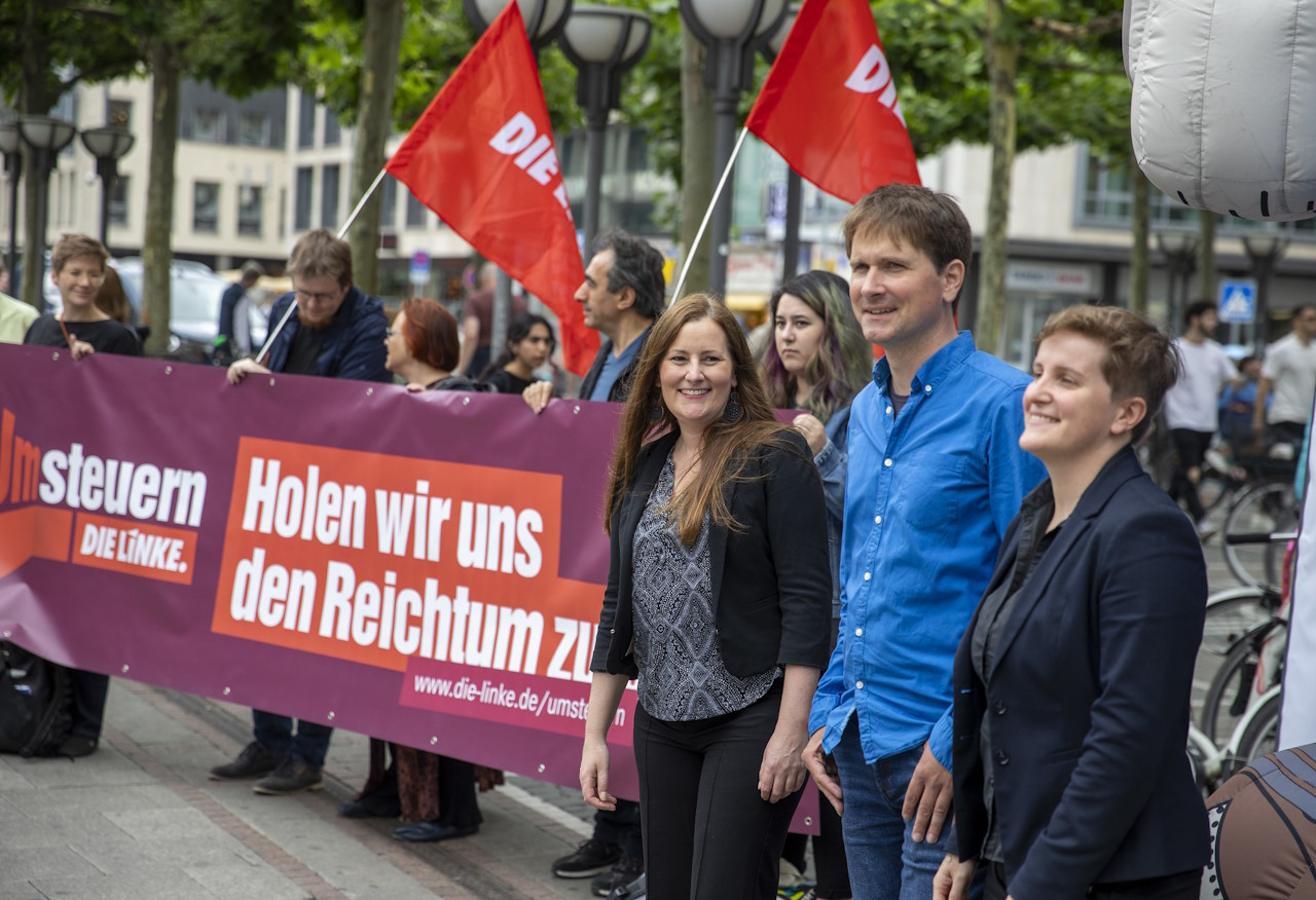Foto von einer Aktion der Partei DIE LINKE in Hessen (Frankfurt am Main), zu sehen sind zwei Fahnen von DIE LINKE sowie Janine Wissler und die beiden Spitzenkandidat*innen zur Landtagswahl 2024 in Hessen