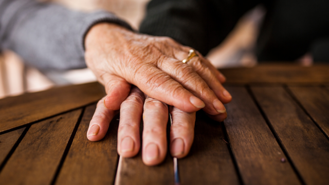 Zwei Hände von zwei älteren Menschen, die auf einem Tisch übereinander liegen.